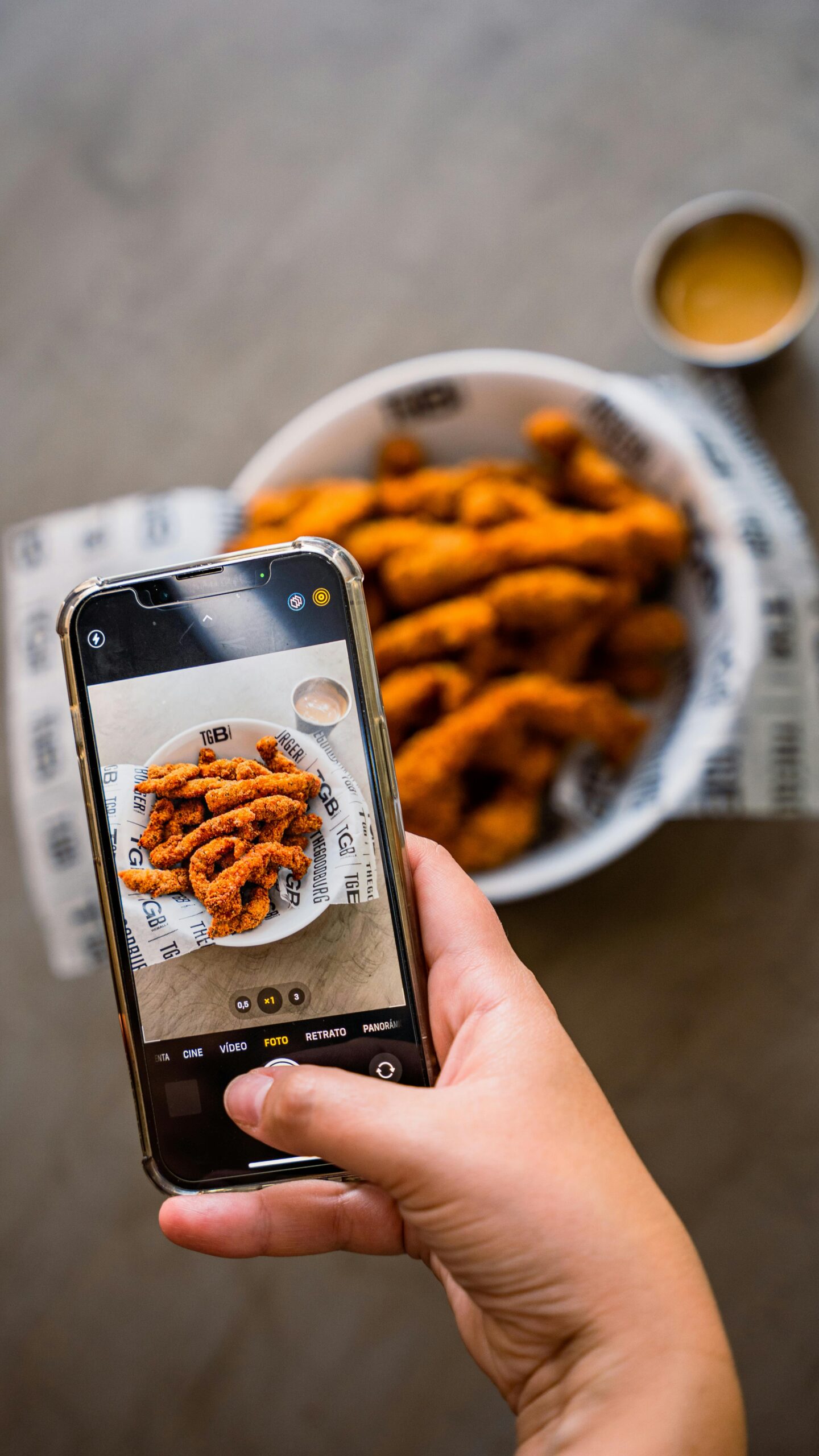 Close-up of hand photographing crispy fried chicken with a smartphone, highlighting food photography techniques.